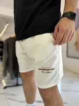 Bermuda de jogging color beige, con bolsillos laterales y estampa con texto blanco en la pierna izquierda.