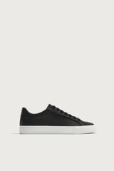 Zapatilla de estilo minimalista con cordones, confeccionada en material sintético liso color negro, con suela de goma blanca texturizada.