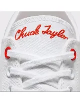 Championes Converse modelo Chuck 70 Ox, de corte bajo, confeccionados en lona blanca con detalles en gamuza gris claro en los laterales. Presentan suela de goma con franjas negras y ojal superior en color rojo.