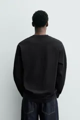 Camiseta de manga larga color negro, corte relajado (relaxed fit) con cuello redondo y un pequeño parche bordado en el pecho con un dado rojo y corazones blancos.