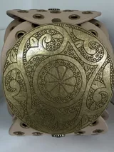 Cinto faja de cuero sintético negro con hebilla metálica dorada con diseño circular calado.