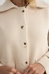 Abrigo de paño negro con cuello camisero, cierre frontal de botones, bolsillos laterales de parche y mangas largas con detalle de botón en los puños.