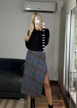 Pollera midi de corte recto con tajo lateral, confeccionada en tela con estampado escocés en tonos marrones, blancos y negros.