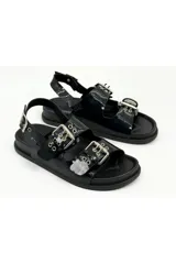 Sandalias negras de charol estilo flatform, con dos tiras frontales con hebillas metálicas grandes y ojales decorativos, y tira trasera con hebilla ajustable.