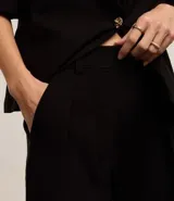 Pantalón de vestir de corte palazzo color negro, con cintura alta, trabillas, cierre tradicional y pliegues.