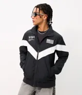 Campera deportiva de poliéster con diseño de bloques de color en negro y blanco. Presenta cuello alto, cierre frontal con cremallera y parches de la NASA y la bandera de Estados Unidos en el pecho.