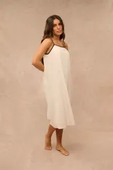 Vestido midi color beige claro con tirantes finos negros y ribete negro en el escote, de corte holgado y fluido.