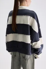 Buzo de estilo rugby con diseño oversize, confeccionado en bloques de color verde militar y celeste con costuras expuestas y deshilachadas. Cuenta con cuello camisero blanco de popelina y cartera de botones frontal oculta, además de mangas largas y puños acanalados.