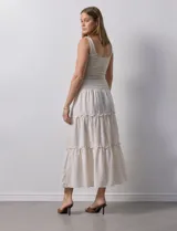 Falda larga de poliéster color beige con finas rayas verticales. Presenta una pretina ancha elastizada con efecto smock y volados en los ruedos de los tres paños que componen la falda.