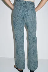 Jeans de tiro alto con corte flare y diseño de tejido jacquard con patrón floral. Presenta cinco bolsillos, trabillas en la cintura y cierre frontal con cremallera y botón.