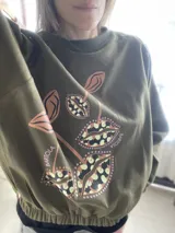 Buzo cropped de algodón color verde militar, con mangas ranglan y diseño estampado en el frente con motivos de besos y moños. Cuenta con elástico holgado en la cintura y los puños.