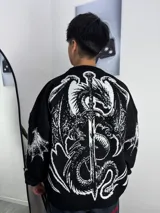 Sweater de tejido de punto color negro con diseño gráfico de un dragón y una espada en color blanco en la espalda y mangas. Presenta cuello redondo y corte holgado.