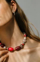Collar corto de diseño artesanal compuesto por cuentas de diversas formas, texturas y materiales en tonos rojo, marrón, beige y blanco, con cadena de ajuste metálica.
