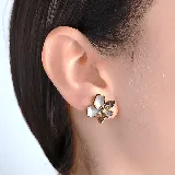 Aros tipo broquel con diseño de flor, elaborados con pétalos de nácar y detalles de cristales en tono ahumado, con engaste en metal dorado.
