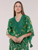 Blusa verde de gasa con transparencia y estampado metalizado dorado, de silueta holgada y mangas cortas. Presenta escote en V con pechera tejida en crochet y apliques de borlas colgantes.