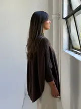 Poncho de punto color chocolate con cuello alto y diseño de trenzas verticales en el frente. Presenta mangas tres cuartos con puños acanalados y un corte holgado y fluido.