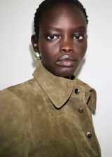Chaqueta corta de piel de serraje color marrón, con diseño recto, cuello camisero, manga larga y cierre frontal de botones metálicos. Cuenta con dos bolsillos de parche con solapa en la parte delantera y forro interior.