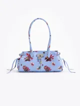 Cartera de hombro de cuero vacuno color celeste con estampado floral multicolor. Cuenta con cierre superior, bolsillo interno, asas largas y detalles de herrajes metálicos con candado y llavero colgante en el frente.