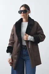 Tapado de efecto cuero negro con interior y detalles de cuello y puños en pelo sintético. Presenta un diseño envolvente con cierre frontal de botones y bolsillos laterales.