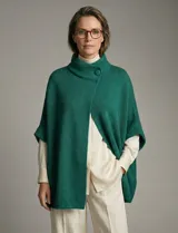 Capa tejida color verde esmeralda, con cuello polera alto que se cierra con un botón grande. Diseño holgado tipo poncho con mangas cortas japonesas.