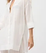 Salida de playa tipo túnica camisera blanca, con mangas 3/4, cuello camisero y cierre frontal con botones. Confeccionada en algodón certificado BCI.