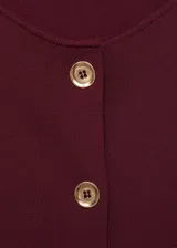 Chaleco de punto fino color bordó, de diseño recto, cuello redondo, sin mangas y cierre frontal con botones dorados.