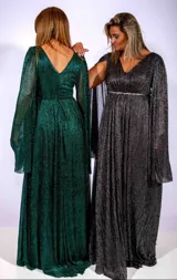 Vestido largo de fiesta en color negro con acabado brillante. Presenta un escote en V, cintura entallada con detalle de cinturón fino y mangas largas tipo capa con efecto plisado.