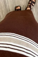 Vestido largo tejido color marrón con rayas horizontales beige y blancas en la parte superior, detalle calado en la parte inferior y tajos a los costados.