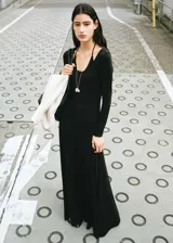 Vestido largo negro de manga larga, con escote redondo y diseño ajustado que se ensancha levemente hacia el suelo.
