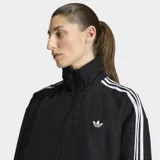 Campera deportiva Adidas modelo Firebird Adilenium, de color negro con las clásicas tres tiras blancas en las mangas, cuello alto y cierre frontal.