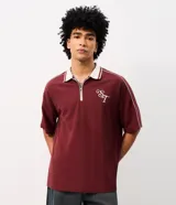 Remera de punto color bordó con ribetes blancos en los hombros y cuello polo, de corte holgado y manga corta. Cuenta con un diseño estampado en la espalda con texto en tonos claros.