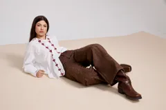 Camisa blanca de corte holgado con cuello camisero y cierre frontal de botones. Presenta un delicado bordado vertical de flores pequeñas en color bordó a lo largo de la botonera y en el cuello.