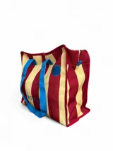 Bolso tote con rayas horizontales rojas y amarillas, asas de mano azules y cierre superior con cremallera.