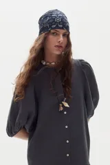 Collar largo estilo artesanal con tira de cuero negra, abalorios de piedra, cuentas de vidrio y dijes colgantes que incluyen una concha marina y un dije metálico alargado.