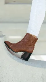 Bota corta de cuero negro con taco cuadrado y punta cuadrada. Presenta un diseño minimalista con costura central vertical y caña media.