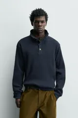 Sudadera de corte relajado confeccionada en tejido de algodón con textura waffle. Presenta cuello subido con cierre frontal de cuatro botones y mangas largas con puños y ruedo en rib.