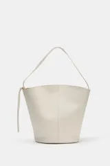 Bolso de hombro de piel en color blanco, con diseño tipo bucket, asa fija y detalle de tira colgante con nudo en el lateral.
