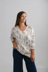 Sweter de punto con diseño estampado tipo nube en tonos azul y gris sobre base beige, con detalles de destellos dorados. Presenta escote en V, corte amplio y mangas largas.