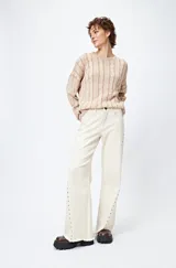 Pantalón de denim corte wide leg color marrón, con ruedo desflecado y detalle de tachas metálicas a lo largo de las costuras laterales.