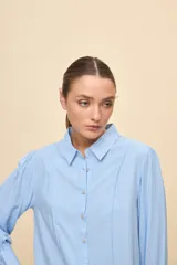 Camisa de manga larga color celeste, con cuello clásico y botonadura frontal. Presenta un calce relajado, con mangas amplias y puños anchos.