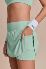Conjunto deportivo compuesto por una pollera short y un top, ambos en color verde menta. La pollera tipo short cuenta con laterales redondeados, bolsillo en la cintura y short interno con bolsillo lateral. El top presenta diseño clásico con escote redondo y tirantes finos.