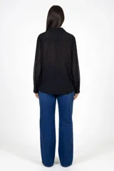 Camisa de corte recto en color negro con estampado de pequeños lunares blancos. Presenta cuello clásico, cierre frontal de botones y mangas largas con puños estructurados.