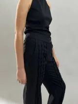 Pantalón tipo babucha confeccionado en lana de oveja, color visón. Presenta un diseño de tiro alto con textura vertical plisada a lo largo de las piernas, cintura con cierre de doble broche y puños elásticos en los tobillos.