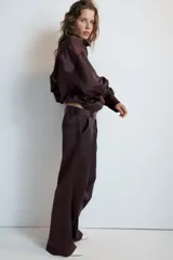 Cazadora satinada de color negro, con cuello subido, manga larga y bolsillos frontales de plastrón con cordones decorativos. Cuenta con bajo elástico y cierre frontal con cremallera y botones a presión oculta.