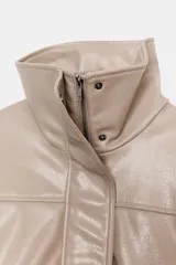 Chaqueta color beige de efecto piel, con cuello subido, manga larga con puño y bolsillos laterales. Tiene forro interior y bajo elástico. Cierre frontal con cremallera y botones a presión ocultos por solapa.