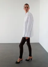 Pantalón slim fit de color marrón oscuro, con diseño largo, cintura elástica y detalle de costuras. Presenta una abertura en el bajo con cierre de cremallera.