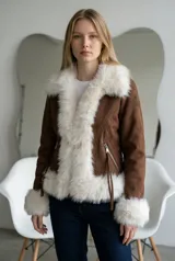 Abrigo de gamuza color marrón con detalles de piel sintética blanca en cuello, solapas, puños y ruedo. Cuenta con cierre frontal y bolsillos laterales con cierre.
