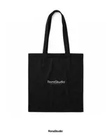 Tote bag negra de lona con estampado gráfico estilo graffiti en color blanco en el frente. Cuenta con dos asas largas para llevar al hombro.