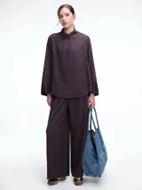 Camisa de corte oversize color bordó, con cuello clásico, cierre frontal de botones y mangas largas amplias con puños anchos. Presenta un diseño de caída fluida con bajo redondeado y levemente más largo en la parte posterior.