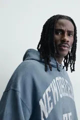 Sudadera tipo hoodie de corte relajado en color azul con efecto lavado. Presenta capucha, mangas largas, puños y ruedo en rib, con estampado frontal en color blanco con texto y números.